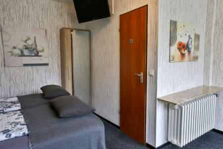 Hotelzimmer mit Doppelbett, Kleiderschrank mit Spiegel, Holztür, Wandbildern und Fernseher.